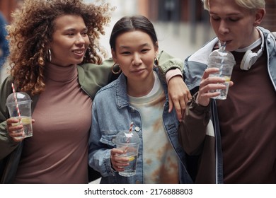 Youthful Guy Drinking Soda Through Sraw While Walking With Two Happy Intercultural Girls Or Coming Back Home After College