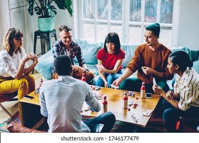 Youthful hipsters with alcohol beverages communicate about blackjack skills during leisure weekend for playing poker, friendly group of hostel guests gambling during cards gaming at gathering party