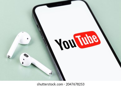 YouTube Mobile Logo App On Screen Smartphone IPhone With AirPods Headphones. YouTube Is A Free Video Sharing Application That Anyone Can Watch. Moscow, Russia -  July 12, 2021