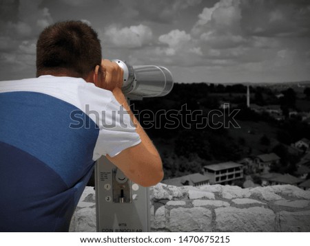 Youung male tourist looks through telescope on city.