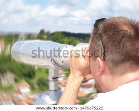 Youung male tourist looks through telescope on city.