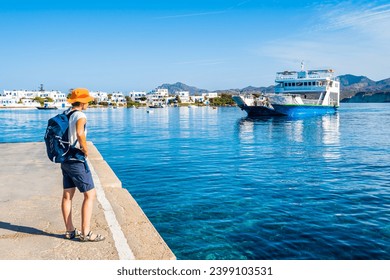 Youung woman tourist with backpack looking at ferry from Kimolos arriving in Pollonia port, Milos island, Cyclades, Greece - Powered by Shutterstock