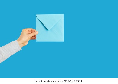 You've Got Mail. Female Hand Holding Square Paper Envelope On Blue Studio Background, Cropped Shot. Courier, Carrier, Mail Woman Delivering Letter With Important Message.Mail And Communication Concept