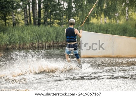 Ypung man wakeboarding and doing different board tricks. Wake boarding sportsman man jumping high wake boarding raley trick with huge water splash in the cable park