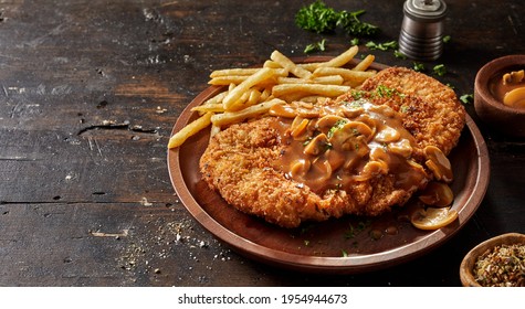 Yummy fried crumbed meat escalope with aromatic chasseur sauce with champignons served with French fries on rustic table