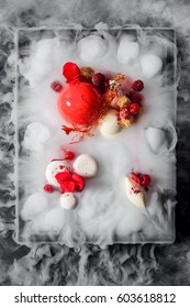 Yummy Mousse Cake, Yogurt Spheres, Cherries, Raspberries, A Caramel Decoration And Fresh Flowers In Dry Ice Mist, A Top-view Image. Molecular Food.
