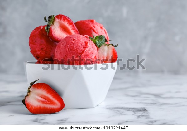 Yummy strawberry ice cream in bowl on white marble\
table. Space for text