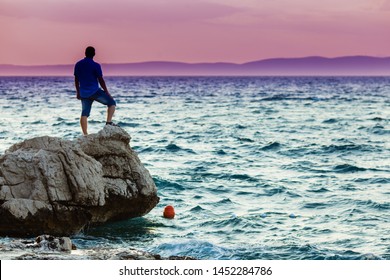 Yung man standing on a rock and looking at the sea sunset
