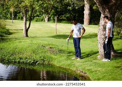 Yup, never getting that back. two men at a water hazard looking for a golf ball.
