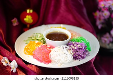 Yusheng, yee sang or yuu sahng, or Prosperity Toss or lo sahng. Placed on white plate and red surfaced table with Chinese decorations.