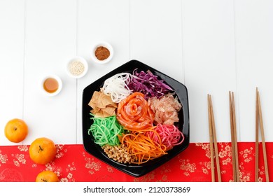Yusheng, Yee Sang or yuu sahng, or Prosperity Toss or Lo Sahng. Placed on Black Plate and White Surfaced Table with Red Chinese Decorations. Copy Space
