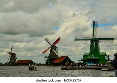 Zaanse Schans, Holland, August 2019. Northeast Amsterdam Is A Small Community Located On The Zaan River. View Of The Mills On The River Bank, They Stand Out With Their Bright Colors. Cloudy Day.