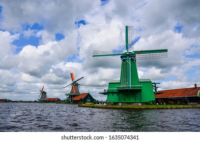 Zaanse Schans, Holland, August 2019. Northeast Amsterdam Is A Small Community Located On The Zaan River. View Of The Mills On The River Bank, They Stand Out With Their Bright Colors. Cloudy Day.