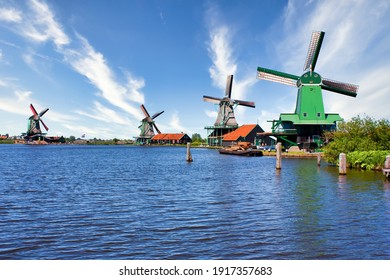 ZAANSE SCHANS, NETHERLANDS - CIRCA AUGUST 2020: Dutch windmill in green countryside close to Amsterdam, with blue sky and river water.