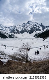 Zakopane, Poland: Panorama Of Morskie Oko Frozen Lake Covered With Snowy Tatra Mountains With People Or Tourists Walking On Snow