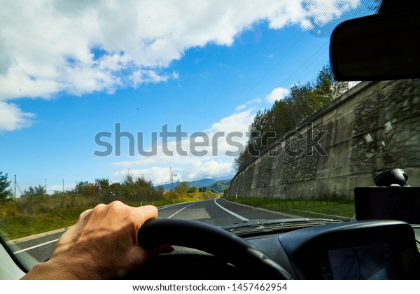 Zakopane, Poland - September 29, 2019: Track from\
the car window and white clouds on blue sky. Woman\'s hand on the\
steering wheel. Female driver seeing beautiful landscape during\
travel in auto