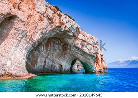 Zakynthos, Greece. Rock arches of Blue Caves from sightseeing boat with tourists in blue water of Ionian Sea. Greece holidays vacation tour with trip from Agios Nikolaos port.