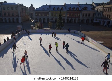 Zamosc, Poland, December 27, 2020. Townspeople Skate On An Ice Skating Rink On A Sunny Winter Morning. Skating Rink In The Central Square Of The City. Urban Winter Fun.