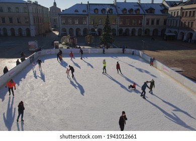 Zamosc, Poland, December 27, 2020. Townspeople Skate On An Ice Skating Rink On A Sunny Winter Morning. Skating Rink In The Central Square Of The City. Urban Winter Fun.