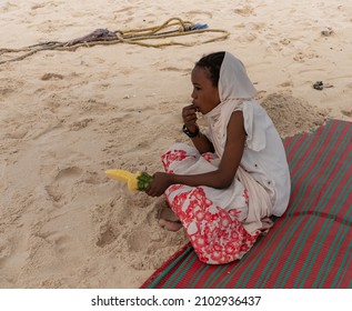 Zanzibar, Tanzania -12.01.2021: Small local African girl eating the middle part of pineapple. Young hungry kid enjoying its lunch on the beach. Moslem girl was given some fresh fruit leftovers