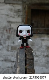 Zaporizhzhia, Ukraine - July 3, 2022: Illustrative Editorial Of Funko Pop Action Figure Of Billy The Puppet From Popular Horror Movie Saw. Toy Standing On Wooden Wheel In Deserted Yard Near Lost Shed.