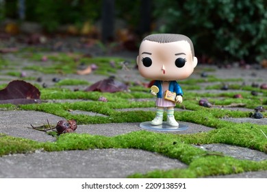 Zaporizhzhia, Ukraine - September 26, 2022: Funko Pop Vinyl Action Figure Of Eleven With Eggo Waffles From Popular Supernatural TV Series Stranger Things. Autumn Garden, Paving Slabs With Green Moss.