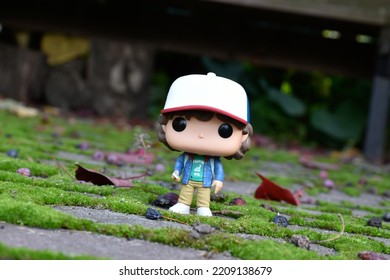 Zaporizhzhia, Ukraine - September 26, 2022: Funko Pop Vinyl Action Figure Of Teenage Boy Dustin Henderson From Popular TV Series Stranger Things. Toy In Autumn Garden, Paving Slabs With Green Moss.