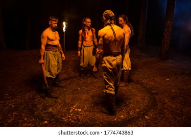 Zaslavl, Belarus, 10.11.2019. Four Men With Athletic Bodies. Dark Night Background. Viking's Nighttime In The Forest Is Lighting By Flamed Torches. 