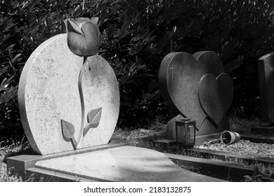 Zeist, Netherlands, 07-2022. The Sun Shines On A Tombstone With A Flower On It. The Photo Is Black And White.