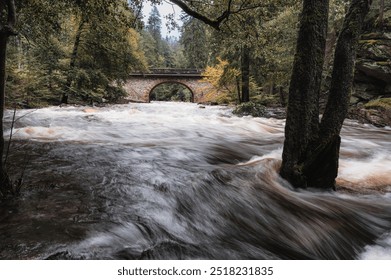 Zemska Brana, old stone bridge over the river Divoka orlice in the valley of the Orlicke mountains. Early Autumn scenery with  trees, stones and wild river after heavy rain. - Powered by Shutterstock