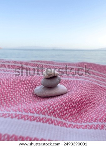 zen, closeup heap or stack of pebble stones on balance on red towel or rug at beach over sea and sky with copy space. zen like balance concept background or surface. stack of small pebble stones