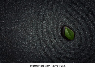 Zen garden with wave lines in the black grain sand with a green leaf - Powered by Shutterstock