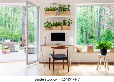 Zen home office with computer in a beautiful, spacious living room interior with plants and an outside view through big windows
