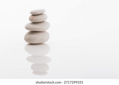 Zen still life featuring a stack of smooth stones balanced precisely on a white surface. The composition evokes peace, tranquility, and a sense of well-being.