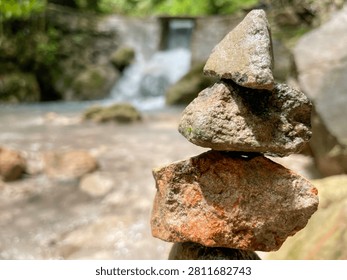 Zen stone stack balanced carefully near a small waterfall in a tropical forest, representing calmness, mindfulness and natural balance surrounded by rocks and greenery