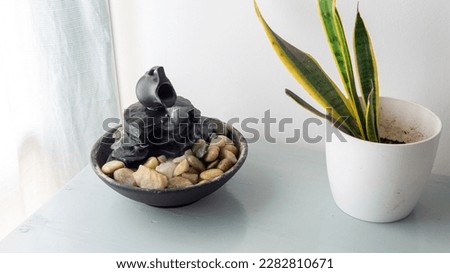 zen water fountain placed on top of a white wooden table next to a window and a green plant in a pot
