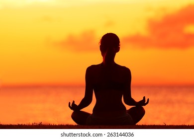 Zen Yoga Woman Doing Meditation On Beach - Wellness Concept. Female Silhouette Relaxing Sitting At Sunset Background Meditating At Ocean Retreat. Summer Orange Sunrise Sky.