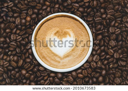 Zenith view of a cup of coffie with a drawn heart  surrounded by coffe beans