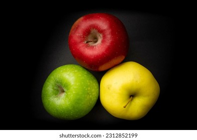 Zenith view of three apples of different colors, yellow, green and red on a black background. Yellow apple, green apple and red apple