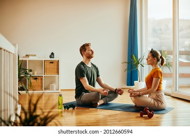 Zen-like couple meditating with their eyes closed while sitting on the floor in the living room. - Powered by Shutterstock