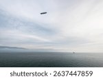 Zeppelin flying over the sea. Wide angle image of a grey airship hovering over Bodensee lake, water surface partially covered in fog, coudy day.