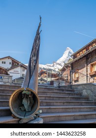 Zermat, Switzerland - May 31st 2019: Alphorn Monument At Zermatt.The Alphorn Or Alpine Horn Is A Labrophone, Consisting Of A Straight Several-meter-long Wooden Natural Horn Of Conical Bore.