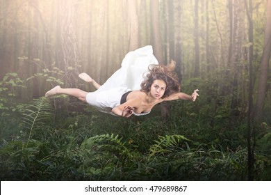 Zero Gravity. Young Beautiful Woman Flying In A Dream. Forest Green And Glow. White Dress And Hair In The Air. Surprise And Light Fright