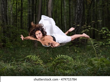 Zero Gravity. Young Beautiful Woman Flying In A Dream In A Summer Forest. White Dress And Hair In The Air. Surprise And Light Fright