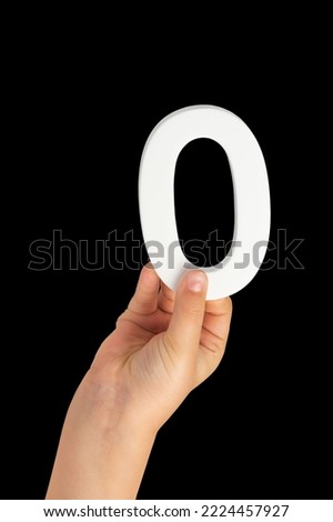 Zero in hand. The number zero is clasped in a hand isolated on a black background. Number zero white in a child's hand on a black background.
