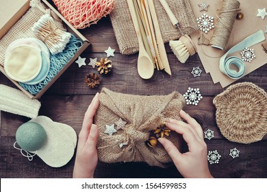 Zero waste christmas. Female hands pack gift wrapped in burlap. Eco friendly products laid out on table