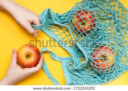 Zero waste concept. Children's hands stack ripe apples in a cotton mesh bag. Top view.