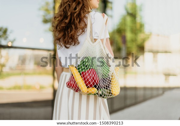 Zero waste
concept with copy space. Woman holding cotton shopper and reusable
mesh shopping bags with vegetables, products. Eco friendly mesh
shopper. Zero waste, plastic free
concept