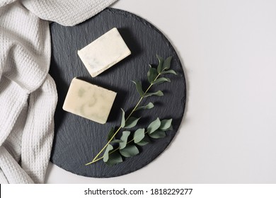 Zero Waste Cosmetics Concept. Flat Lay, Top View Of Natural, Organic Solid Handmade Soap And Eucalyptus Plant Near Towel On Black Plate Stand Against White Copy Space Background