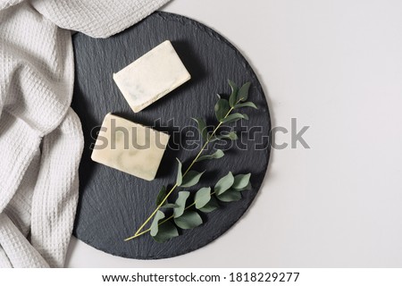 Zero waste cosmetics concept. Flat lay, top view of natural, organic solid handmade soap and eucalyptus plant near towel on black plate stand against white copy space background